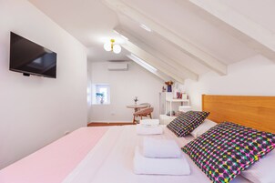 Quarto moderno com cama grande, televisão na parede, mesa pequena e janela.