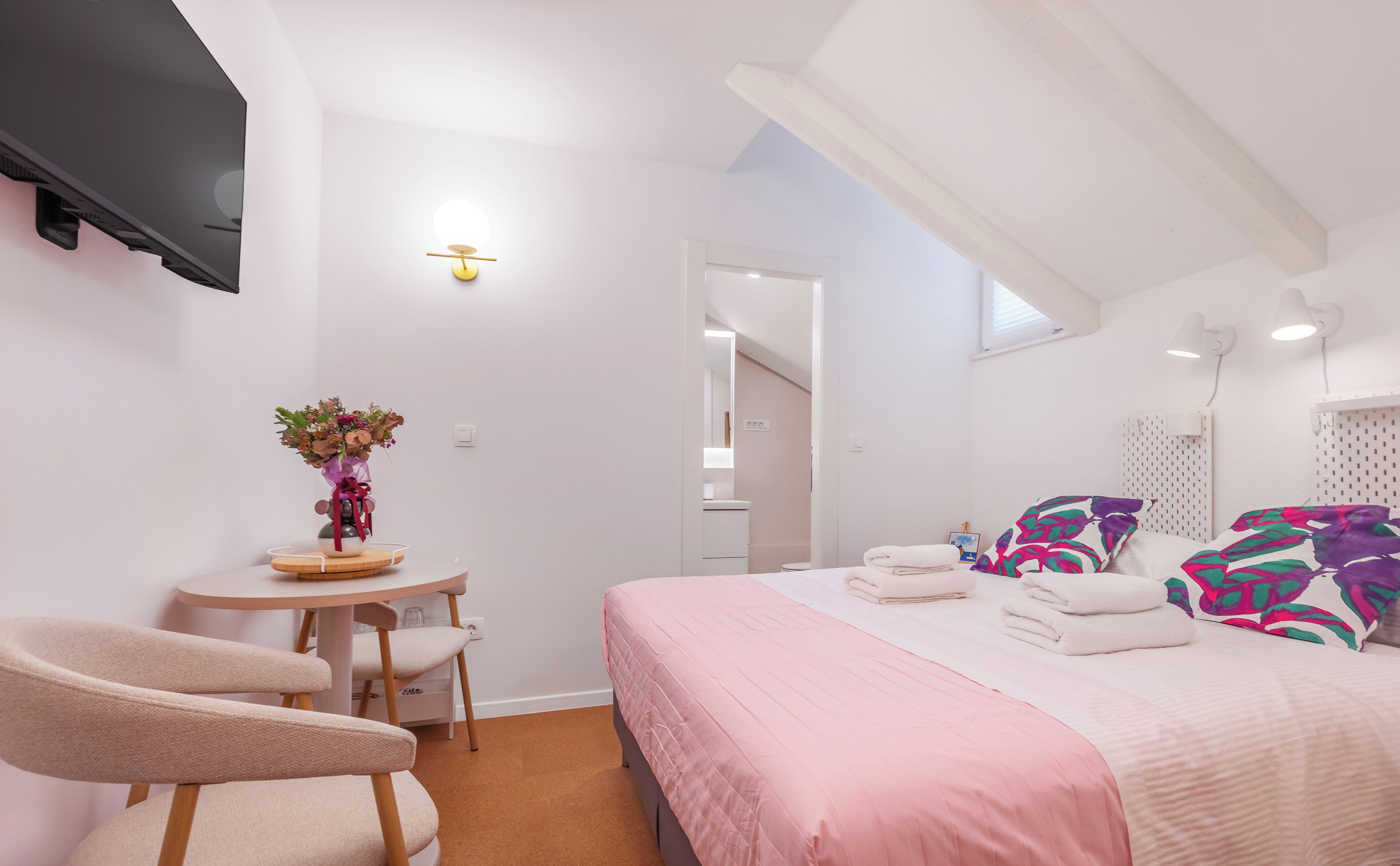 A modern bedroom with a bed, bedside tables, a chair, a desk, and a vase of flowers.