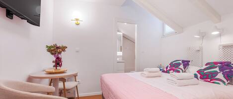 A modern bedroom with a bed, bedside tables, a chair, a desk, and a vase of flowers.