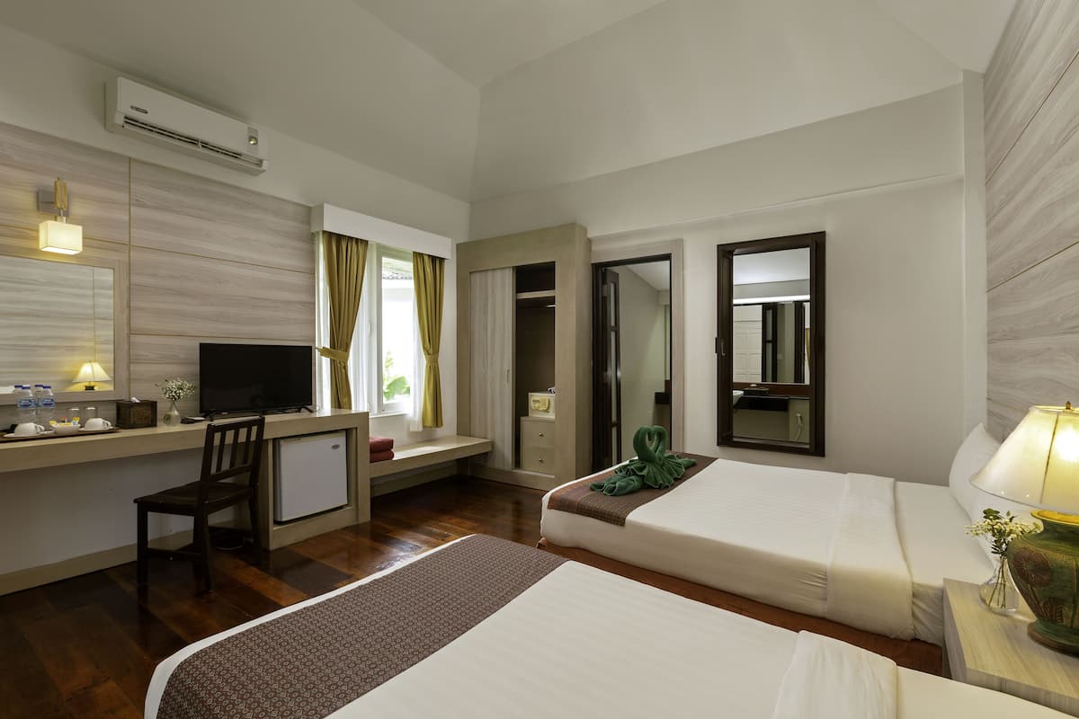 Une chambre d’hôtel avec deux lits, un bureau avec une télévision, une petite kitchenette et une salle de bain visible par une porte ouverte.