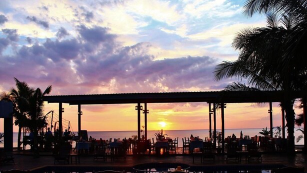 A sunset view from a covered outdoor seating area with a pool.