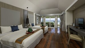 A modern hotel room with two beds, a desk, and a TV. The room has a balcony with a view of the sea.