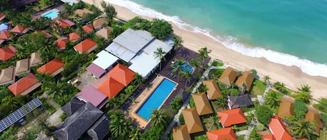 An aerial view of a resort with multiple buildings, a swimming pool, and a beach.
