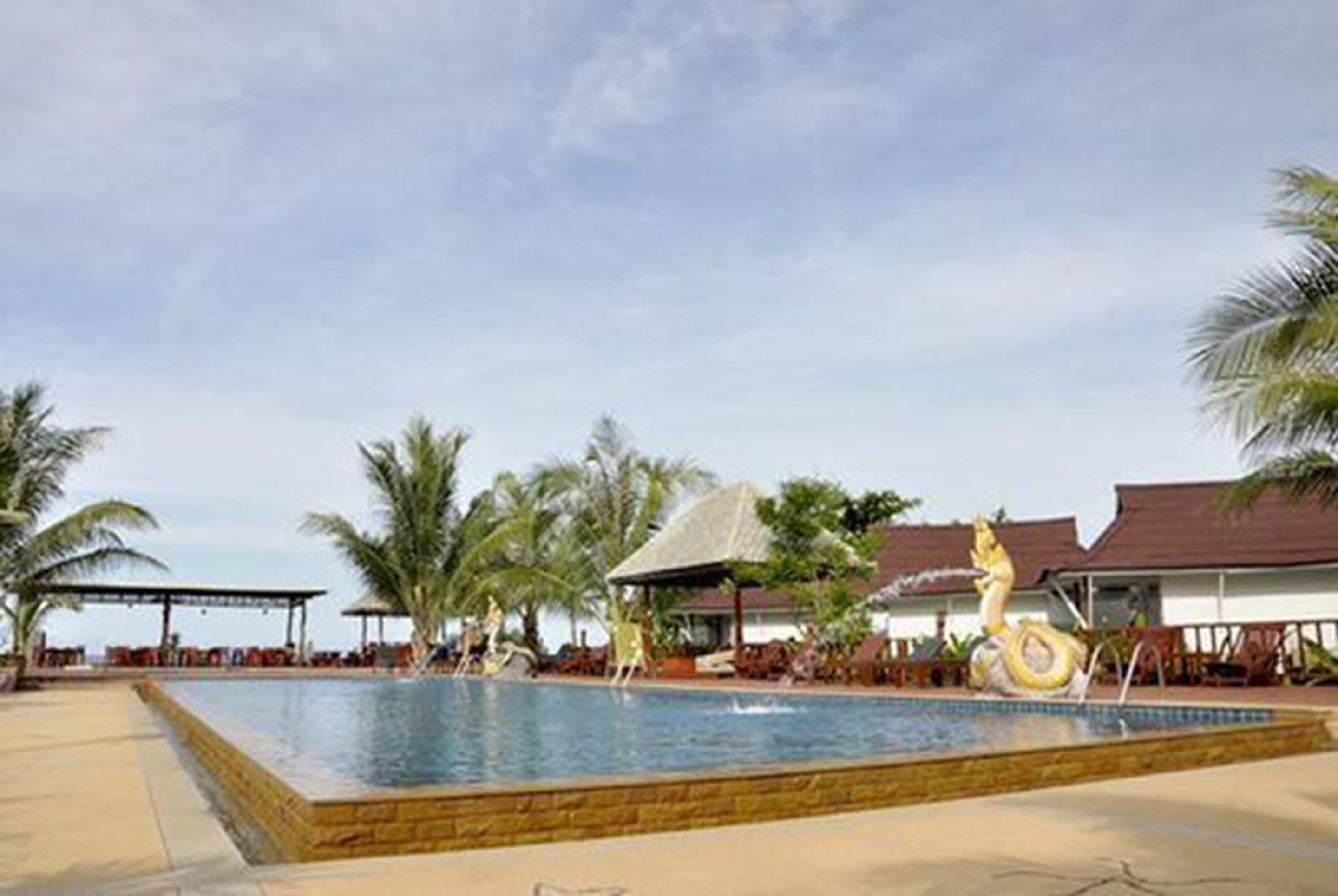 A swimming pool with a decorative sculpture, surrounded by palm trees and covered seating areas.