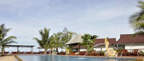 A swimming pool with a decorative sculpture, surrounded by palm trees and covered seating areas.