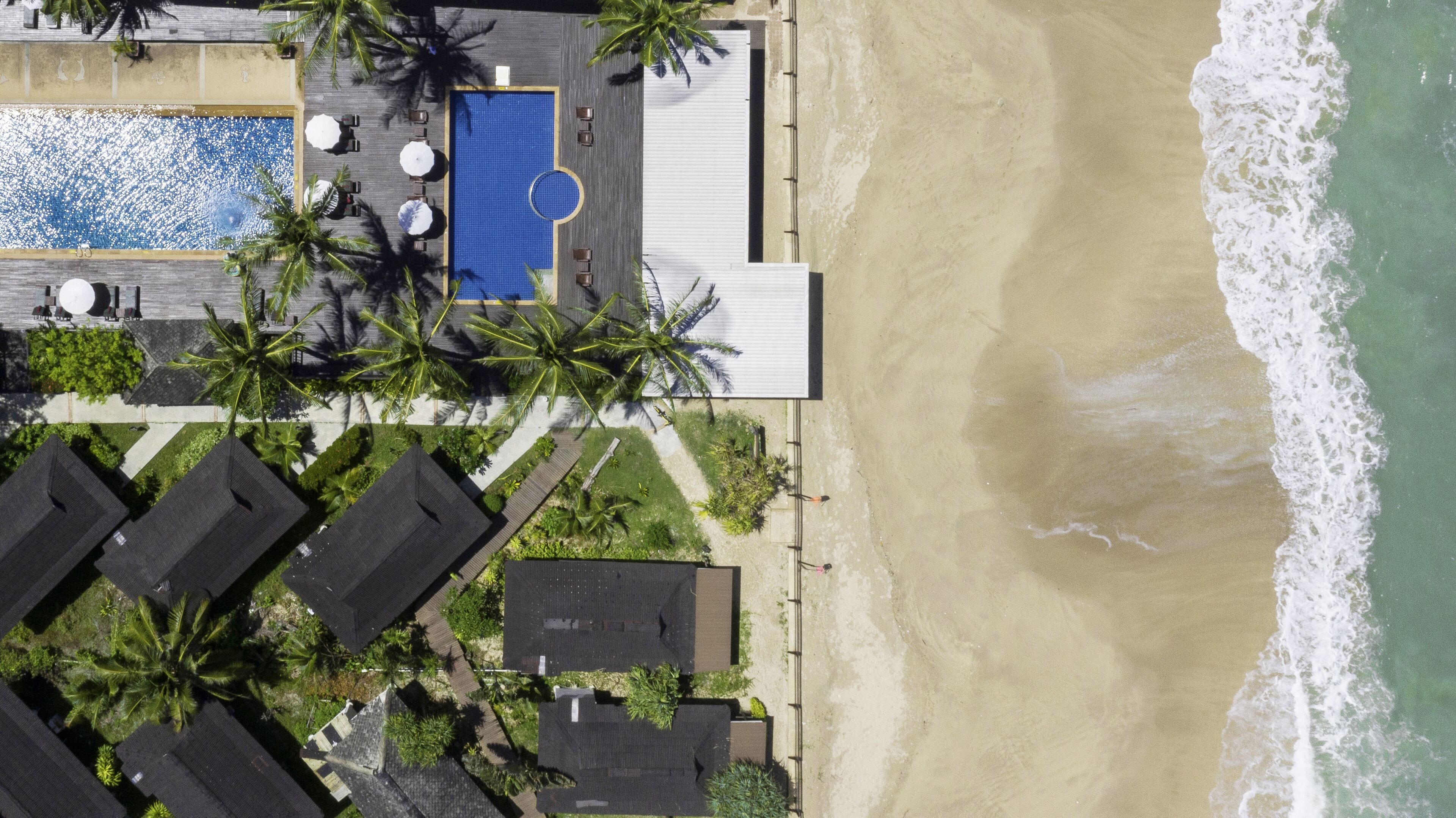 An aerial view of a beachfront property with a swimming pool, lounge area, and multiple bungalow-style accommodations.