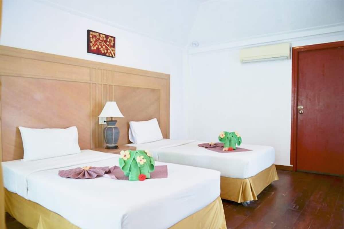 Une chambre d’hôtel avec deux lits, une tête de lit en bois, un climatiseur fixé au mur et une porte.