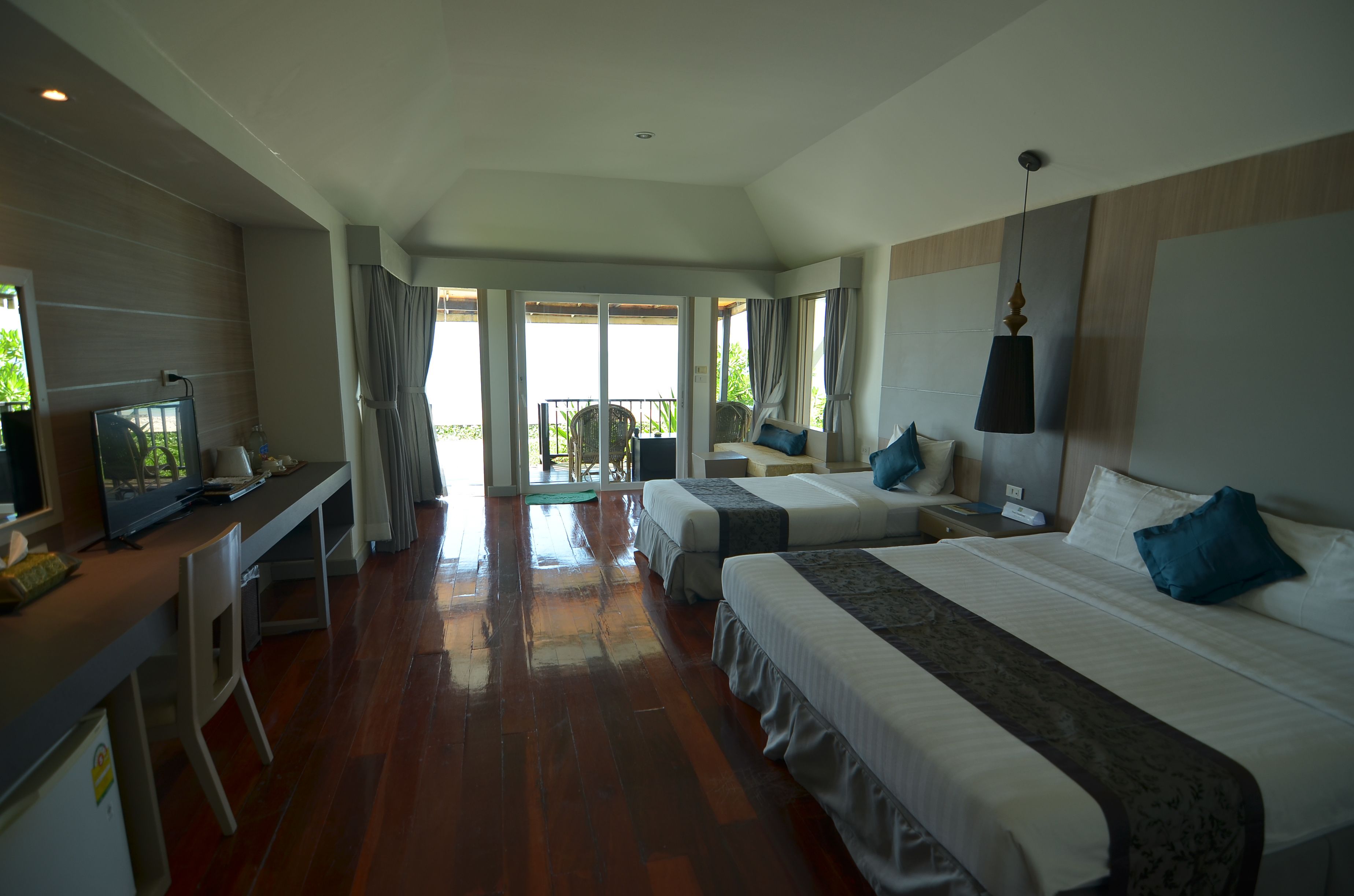 A hotel room with two beds, a desk with a television, and a balcony with a view.
