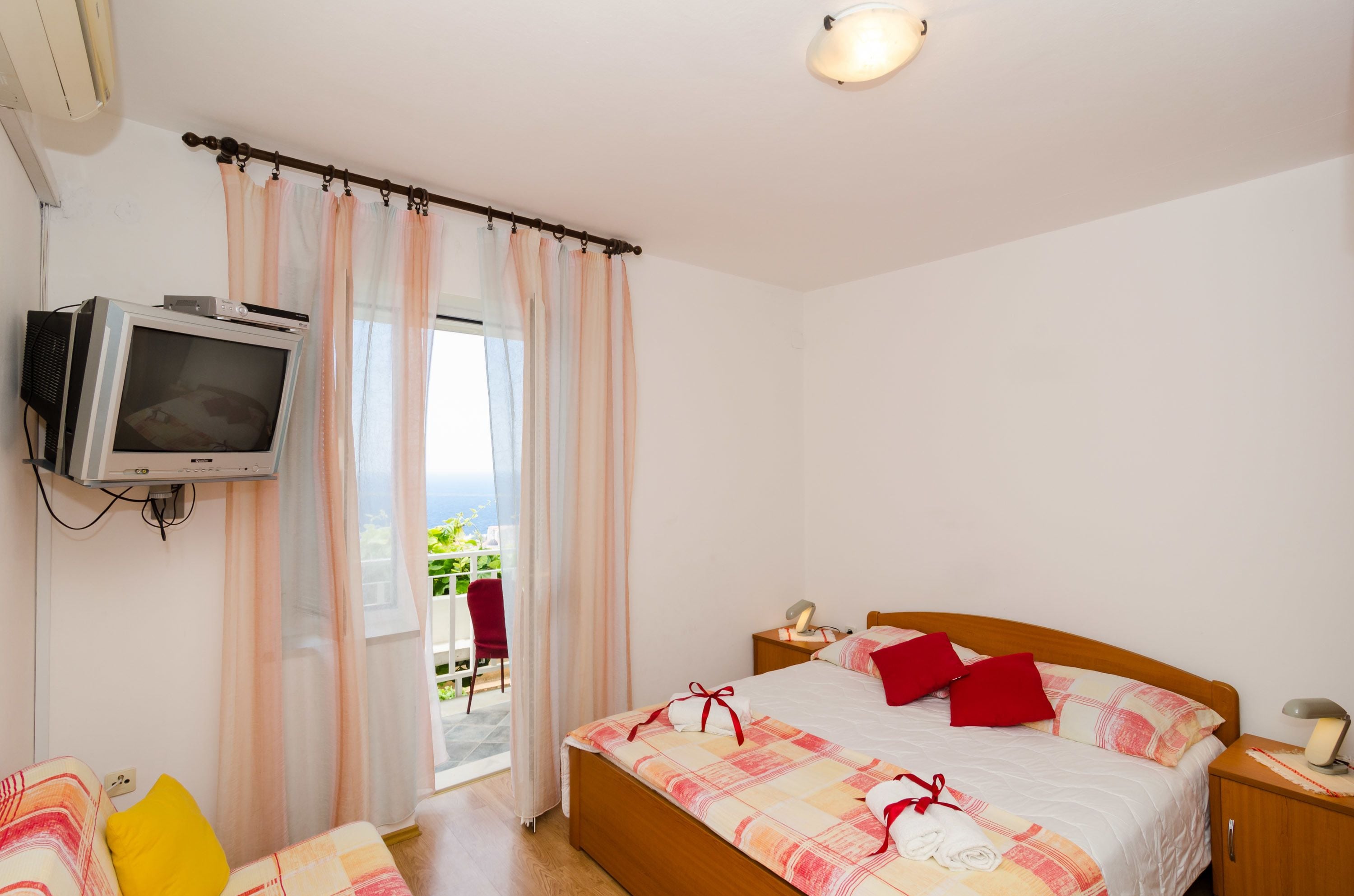 A bedroom with a bed, a bedside table, a TV mounted on the wall, and a view of the outdoors.
