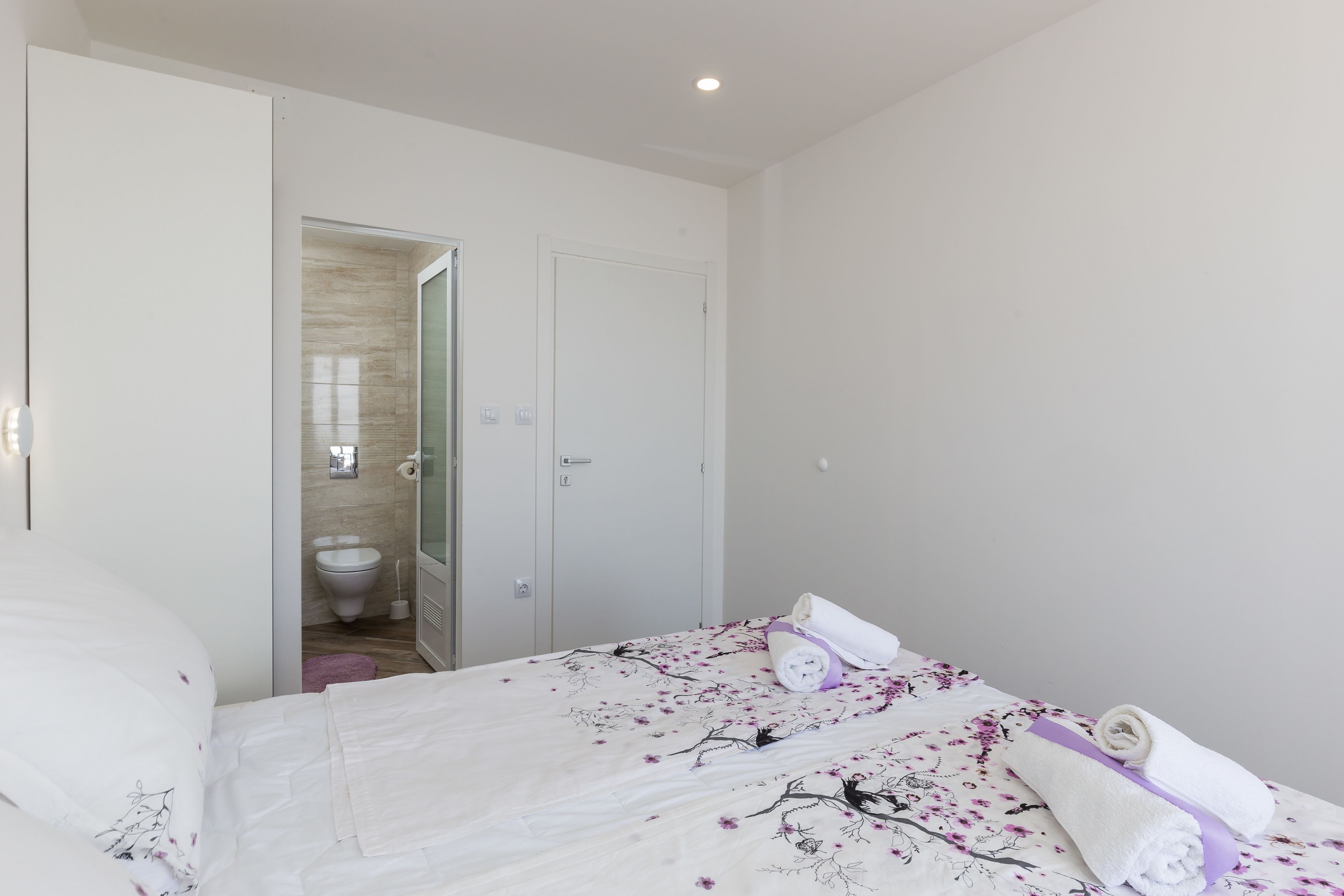 A bedroom with a bed, a bathroom visible through an open door, and a towel on the bed.