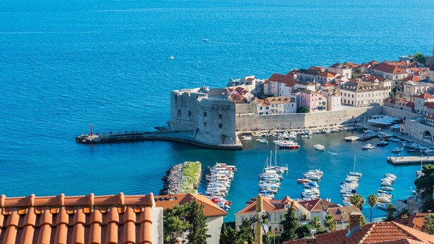 A coastal town with a historic fort, a marina with boats, and buildings with red-tiled roofs. - Guesthouse Home Sweet Home (Dubrovnik)