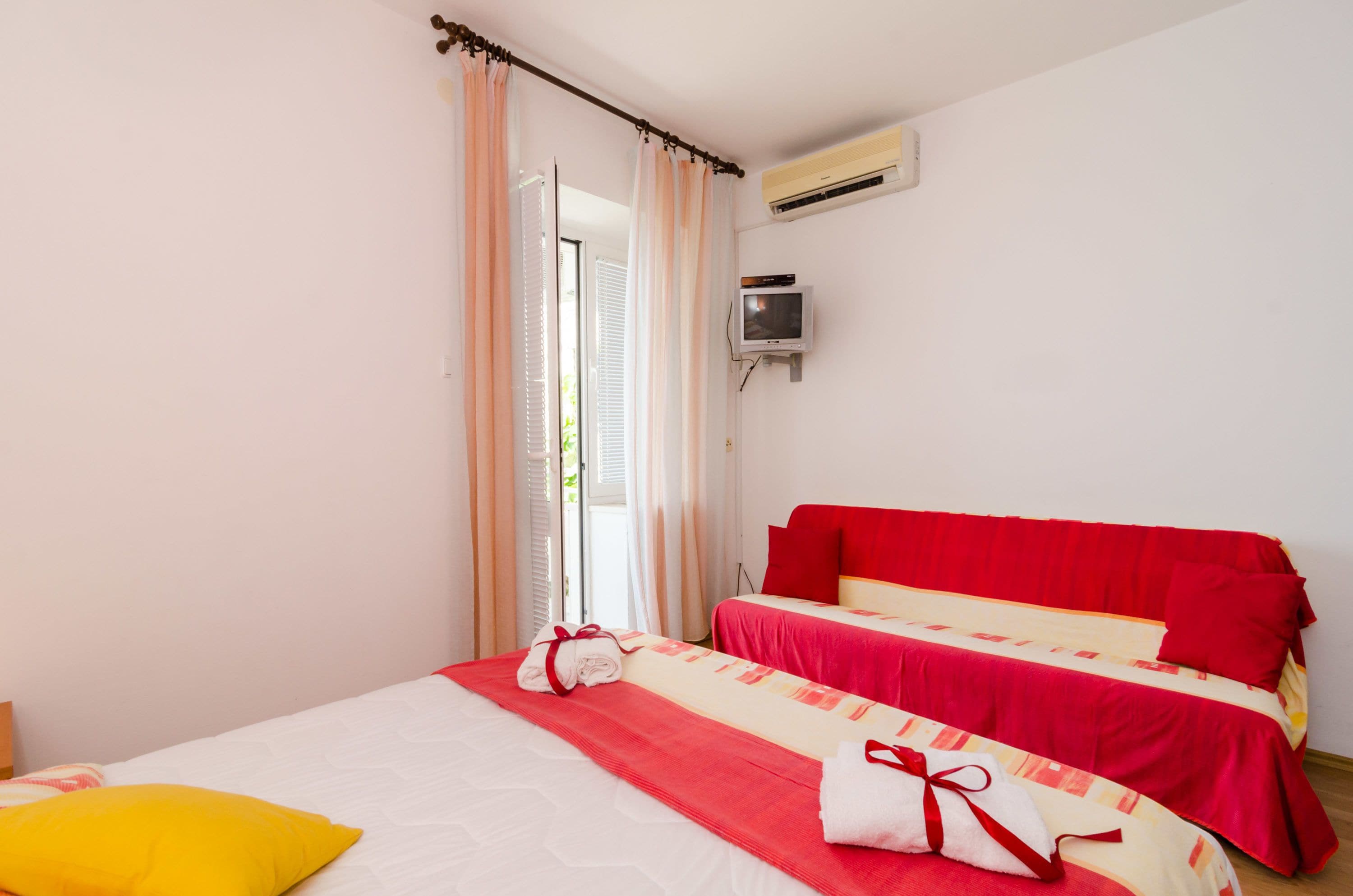 A hotel room with two beds, a TV, and an air conditioning unit.