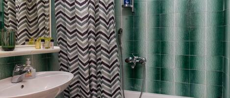 Un baño con un lavabo blanco, paredes con azulejos verdes, una ducha con cortina a rayas y una bañera.