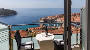 A balcony with a table and chairs, overlooking a coastal town with a historic fort and red-roofed buildings. - Guesthouse Home Sweet Home (Dubrovnik)