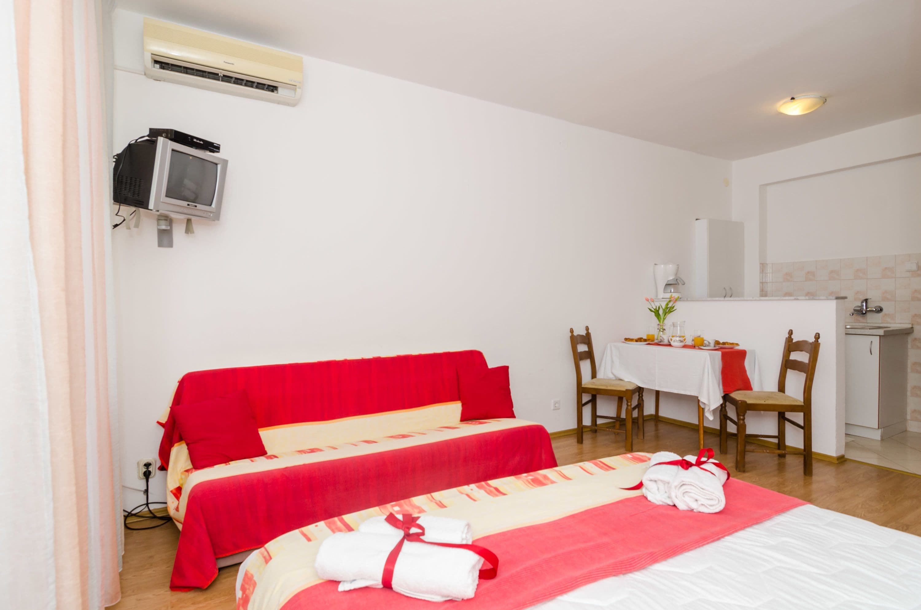 A hotel room with two beds, a small kitchenette, and a TV mounted on the wall.