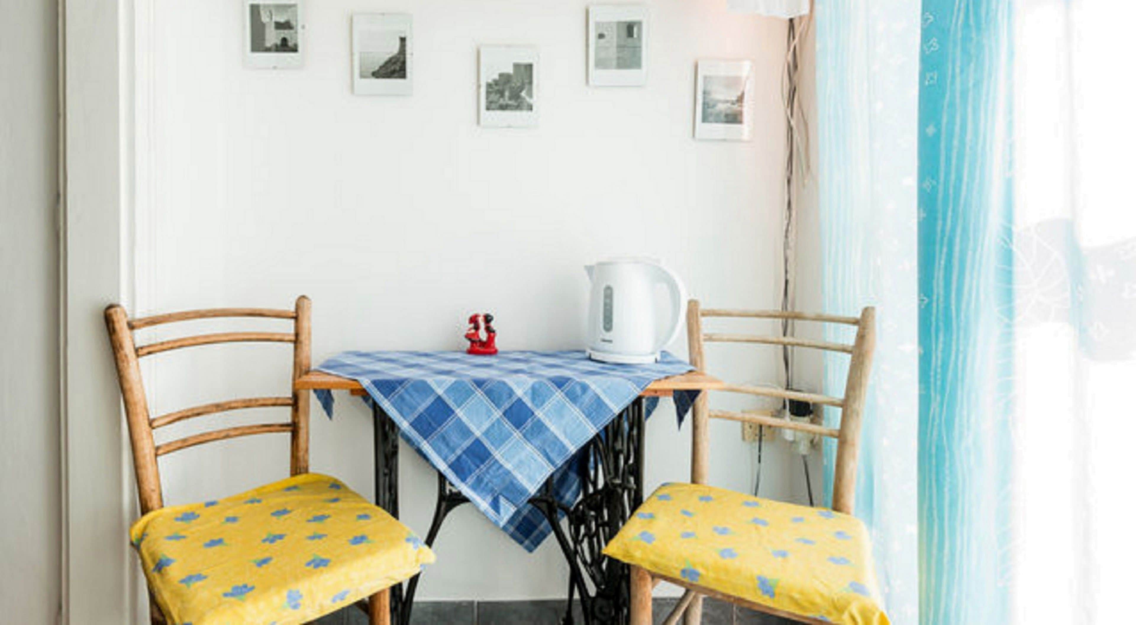 A dining area with two wooden chairs, a table covered with a blue checkered tablecloth, and a white kettle.