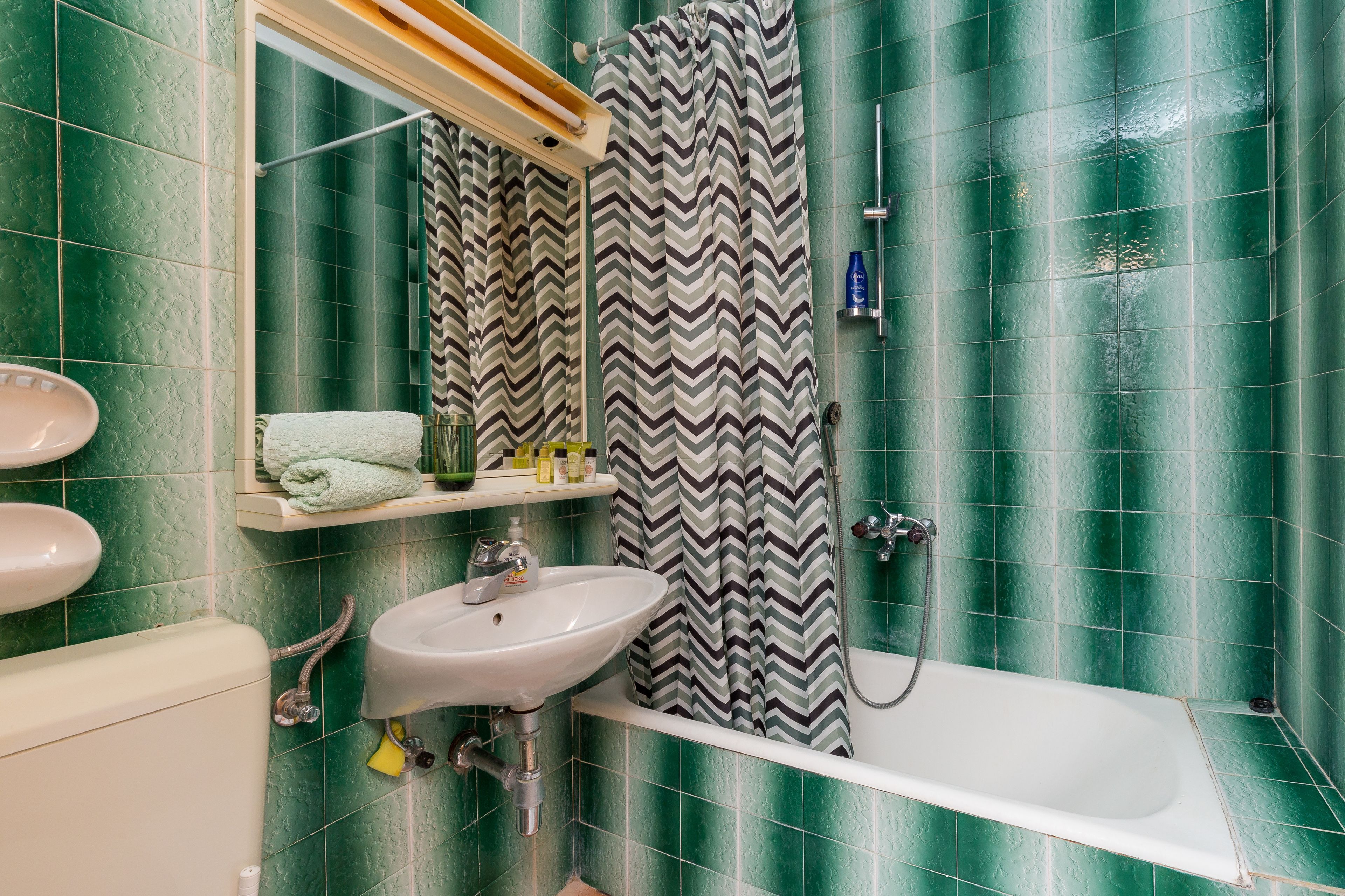 A bathroom with green tiles, a white sink, a bathtub, and a shower curtain.