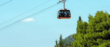 A cable car in motion against a clear sky, with dense green trees and a distant building visible.