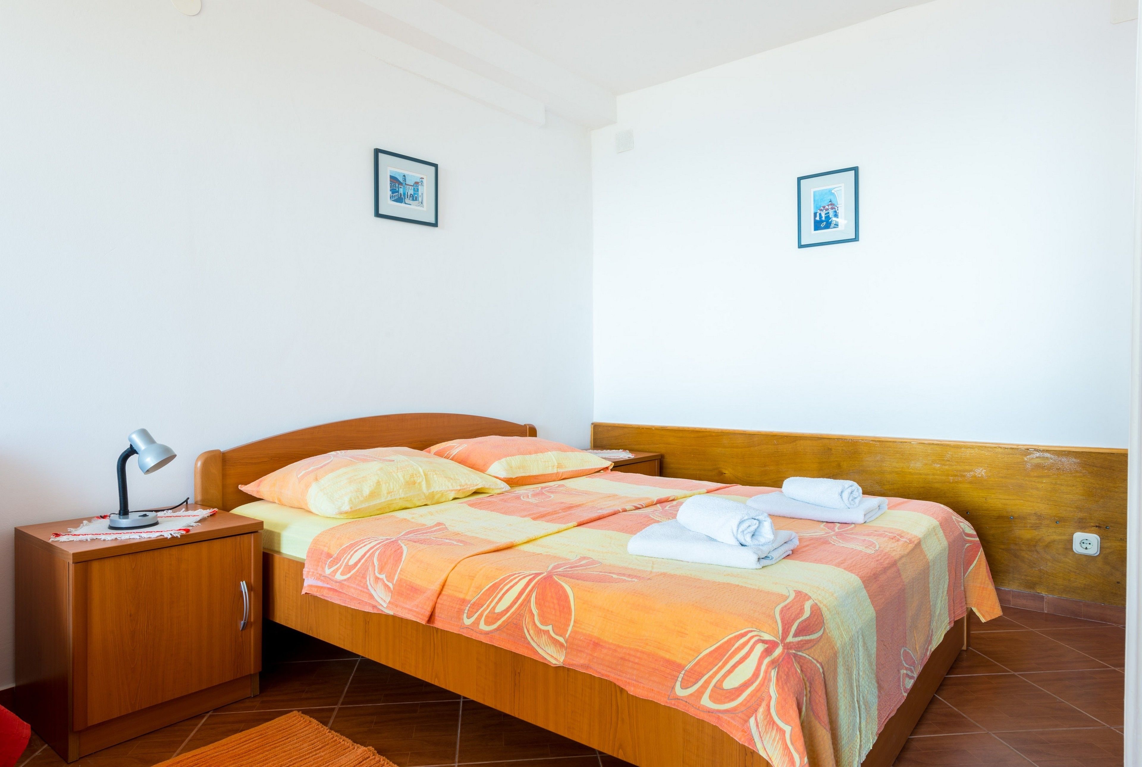 A bedroom with a wooden bed, a nightstand with a lamp, and two framed pictures on the wall.