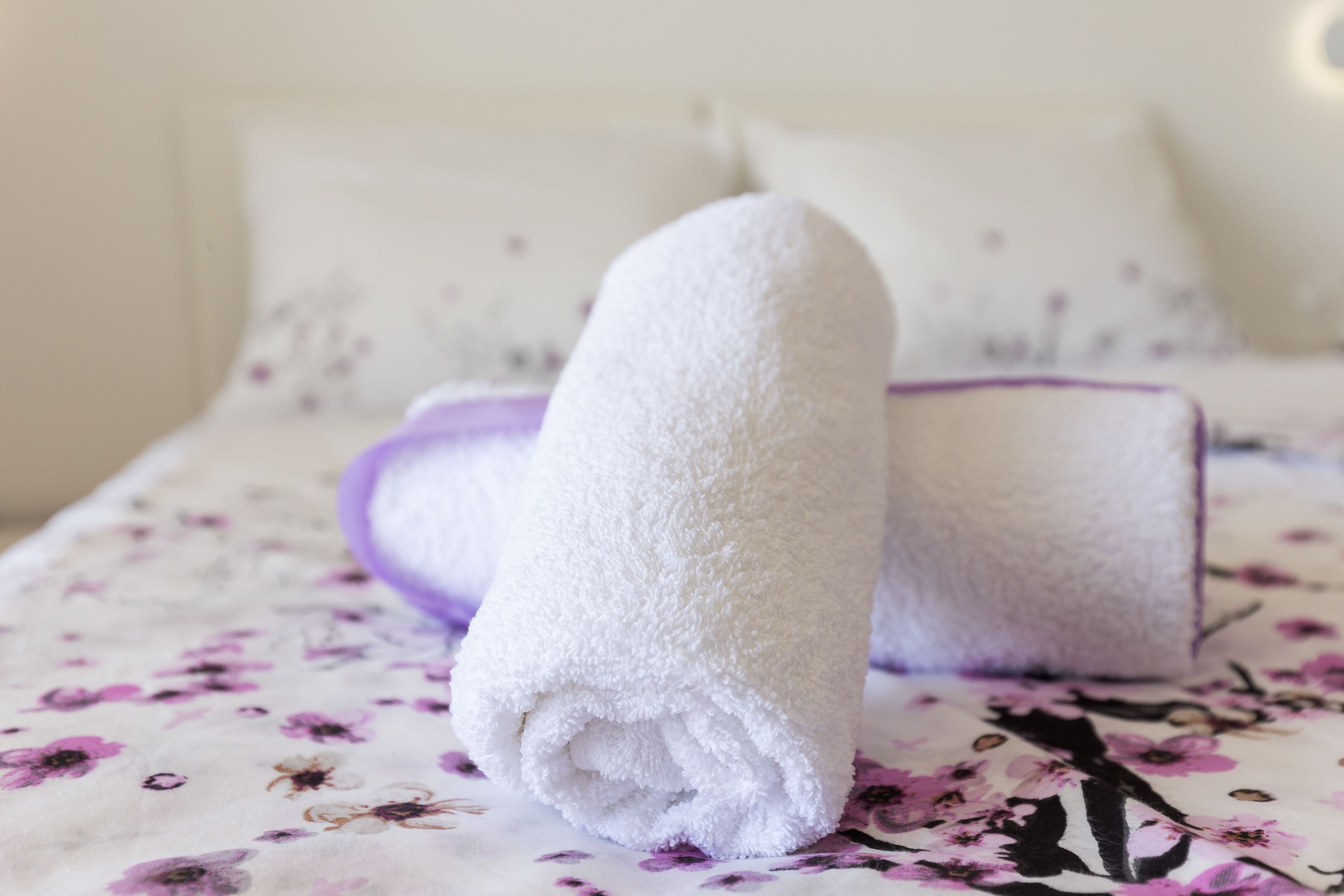 A neatly made bed with a floral-patterned bedspread and two rolled white towels placed on it.