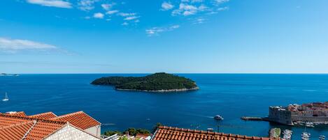 A coastal town with terracotta-roofed buildings, a small island, and clear blue skies.