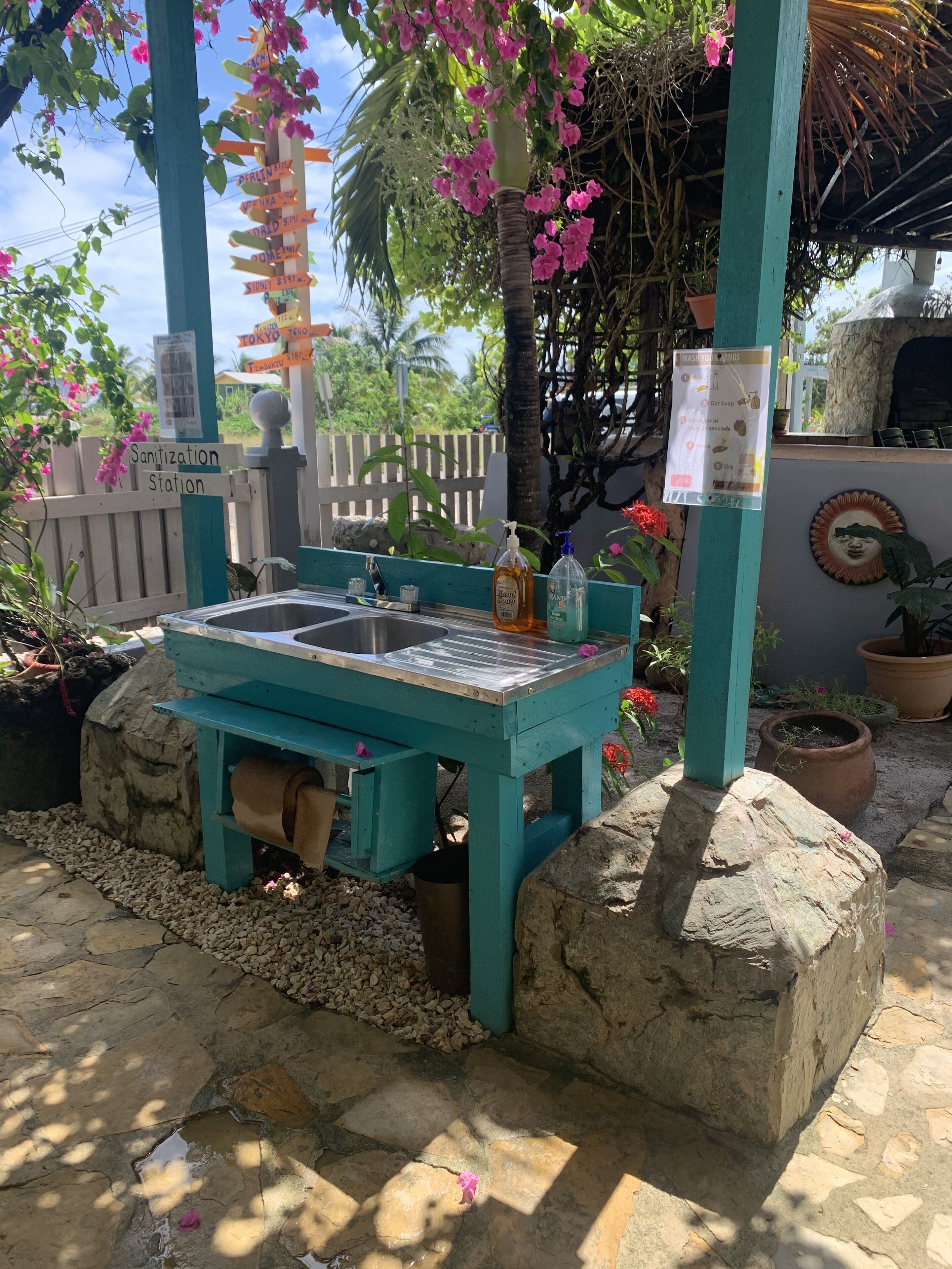 A turquoise outdoor washbasin with a hand soap dispenser, surrounded by pebbles and a stone wall.