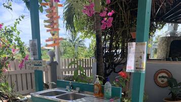 A turquoise outdoor washbasin with a hand soap dispenser, surrounded by pebbles and a stone wall.
