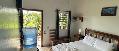 A bedroom with a bed, a ceiling fan, a water dispenser, a wooden headboard, a nightstand, and a painting on the wall.