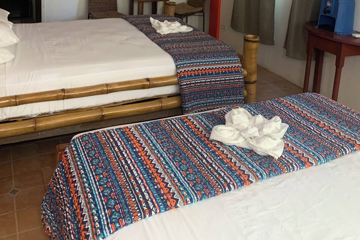 A hotel room with two beds, a ceiling fan, a water dispenser, and a painting on the wall.