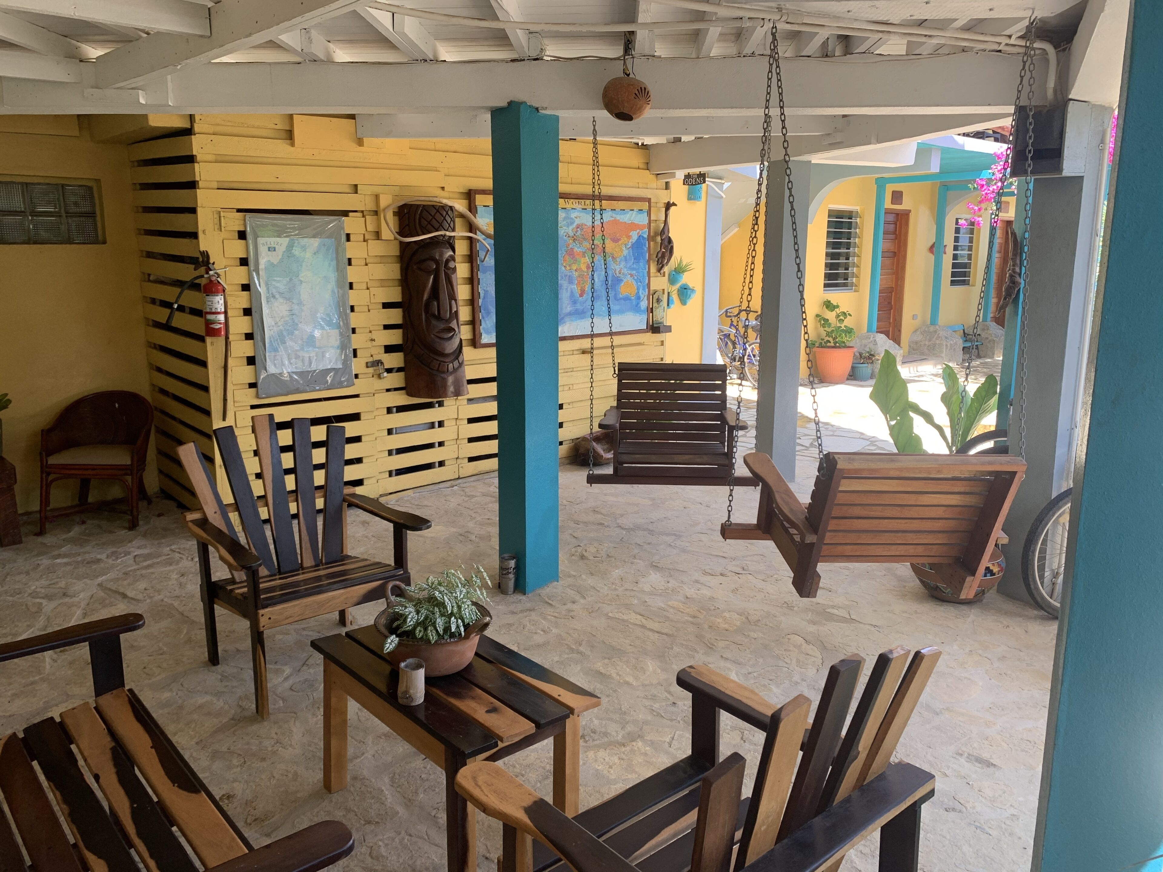 A covered outdoor seating area with wooden benches and chairs, a map, and a wooden sculpture.