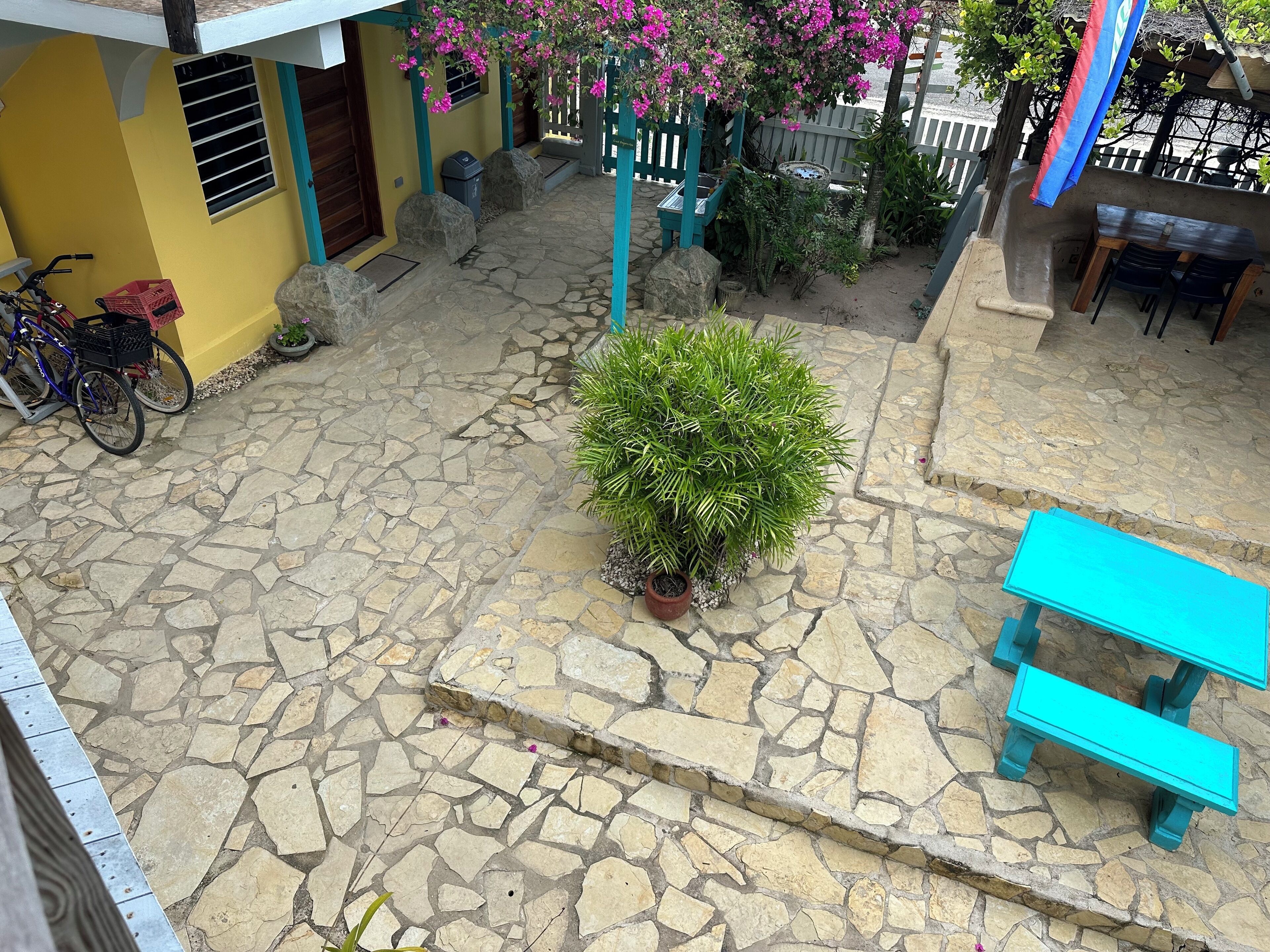 Une cour avec un sol en pierre, une petite plante en pot, un vélo et une table avec des chaises.