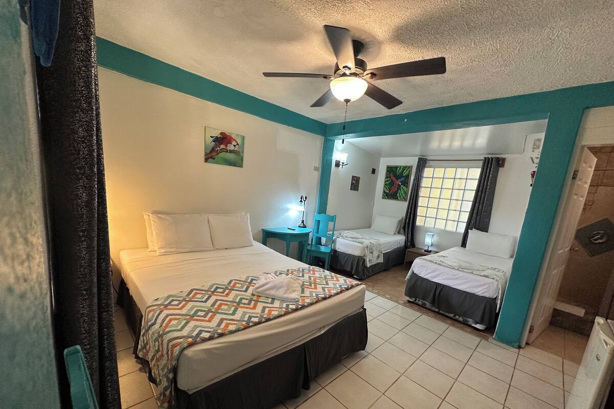 A hotel room with two beds, a ceiling fan, a window with curtains, and a tiled floor.