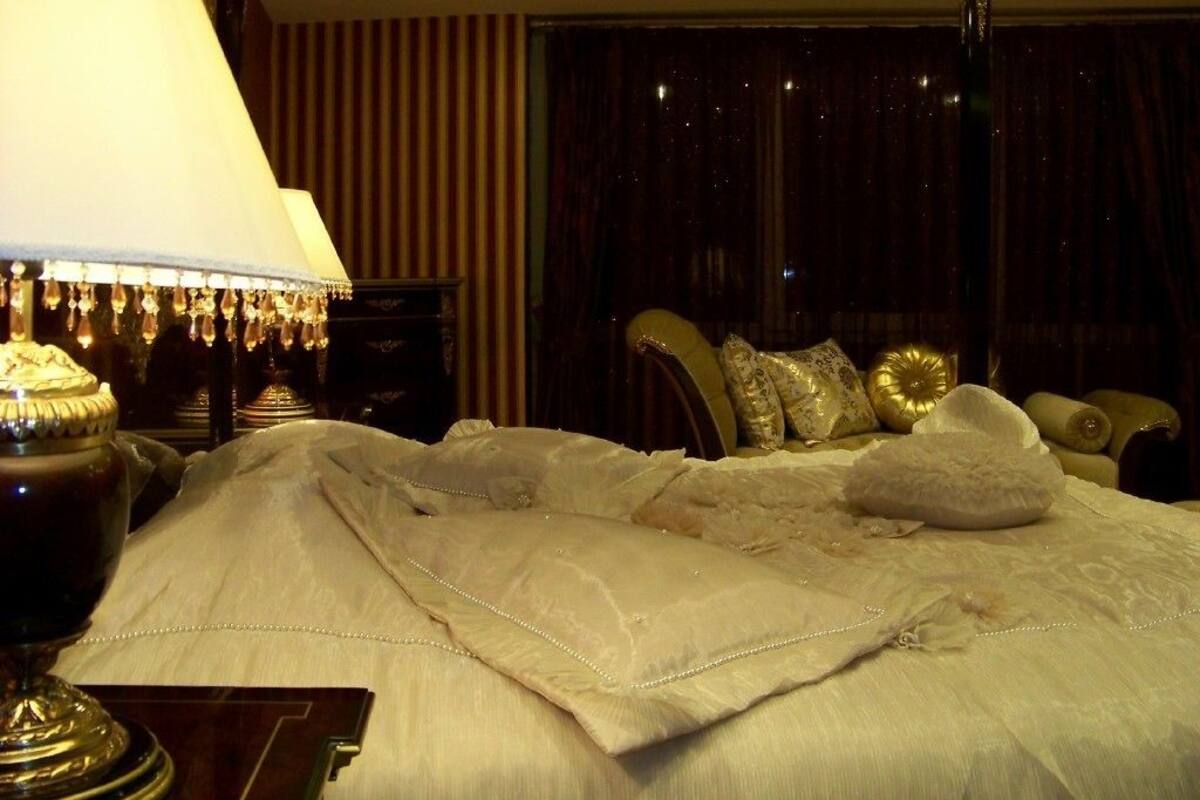 Een hotelkamer met een groot bed, een bedlampje en een donkere gordijnen achtergrond.