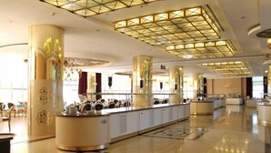 Un hall d’hôtel spacieux avec un buffet central, de grandes colonnes décoratives et un plafond au design géométrique.
