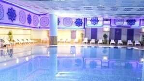 Une grande piscine intérieure dotée de chaises longues et ornée de motifs décoratifs sur les murs.