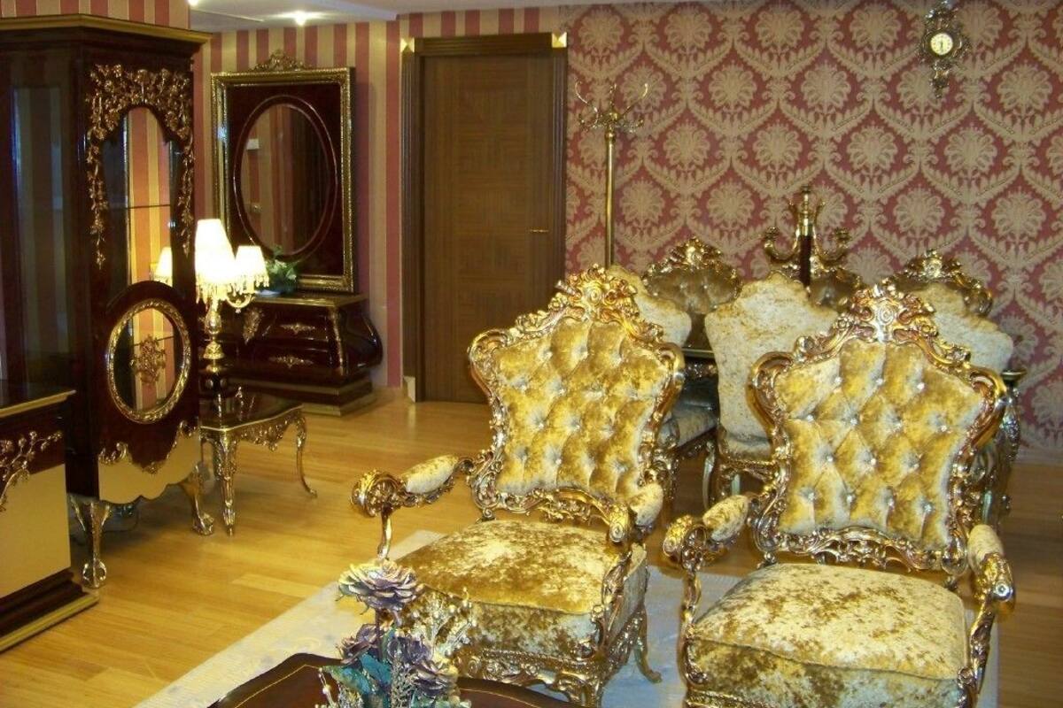 Een kamer met sierlijke, goud- en wit beklede stoelen, een grote spiegel en behang met een patroon.