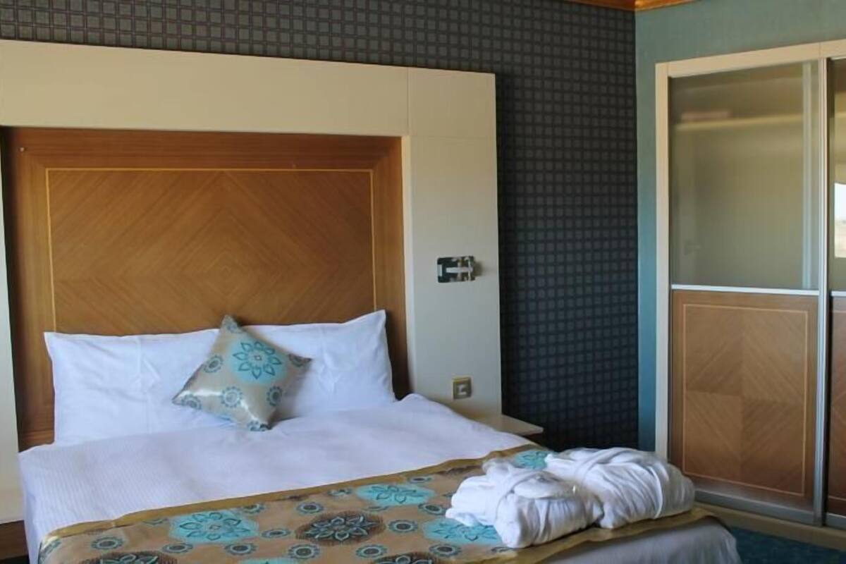 Een hotelkamer met een groot bed, een houten hoofdeinde, een kledingkast met uitzicht en een geborduurde spreidekker.