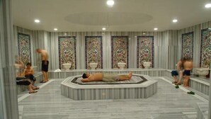 Une salle de spa dotée d’un grand jacuzzi central, d’un sol en marbre et de panneaux muraux décoratifs.
