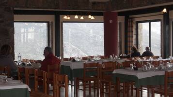 A restaurant with multiple tables and chairs, large windows with a mountain view, and a stone wall interior.