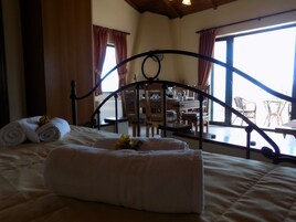Un dormitorio con cama, cabecera de madera y vistas a un área de estar exterior a través de amplios ventanales.