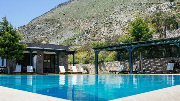 Ein Pool mit Liegestühlen und einem Pavillon, umgeben von einer Steinmauer und einem Bergpanorama.