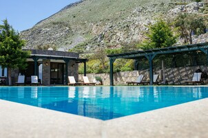 Una piscina con sillones de descanso y un pabellón, rodeada por un muro de piedra y con montañas al fondo.