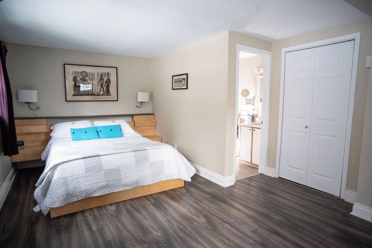 A bedroom with a wooden bed, two bedside lamps, a framed picture on the wall, and a white door.