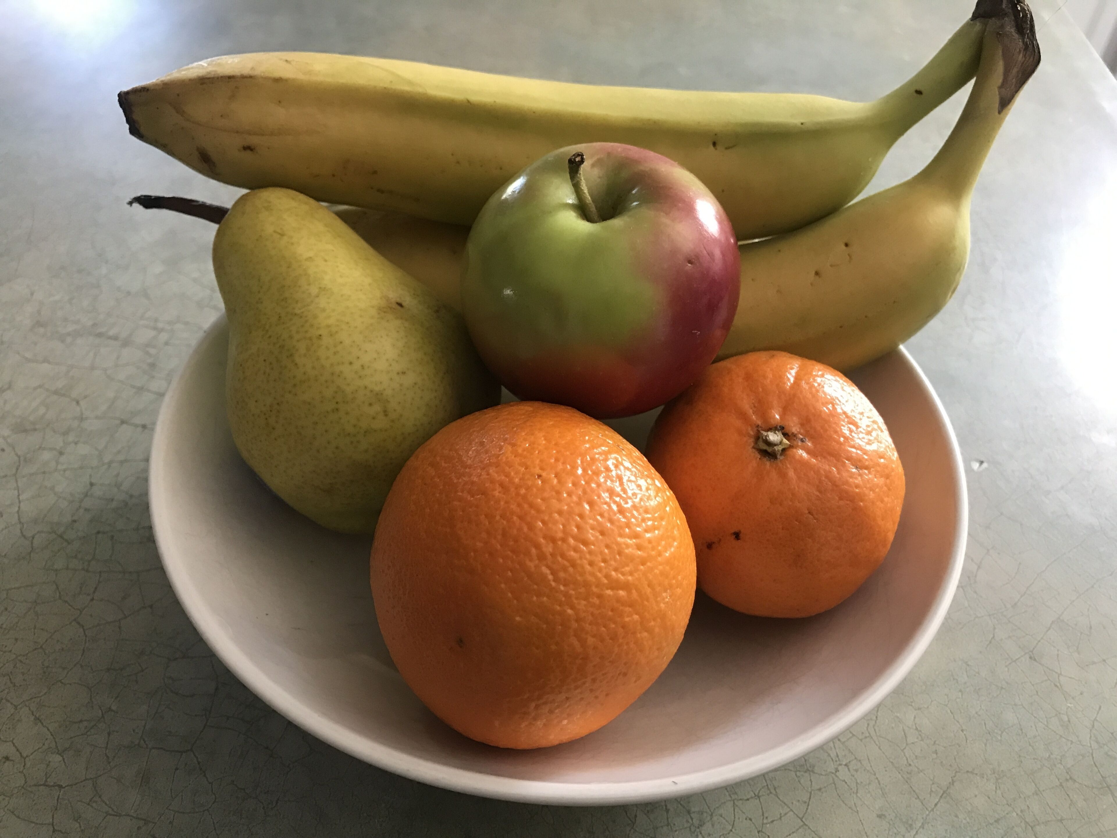 Une assiette avec une poire, une pomme, deux oranges et une grappe de bananes.