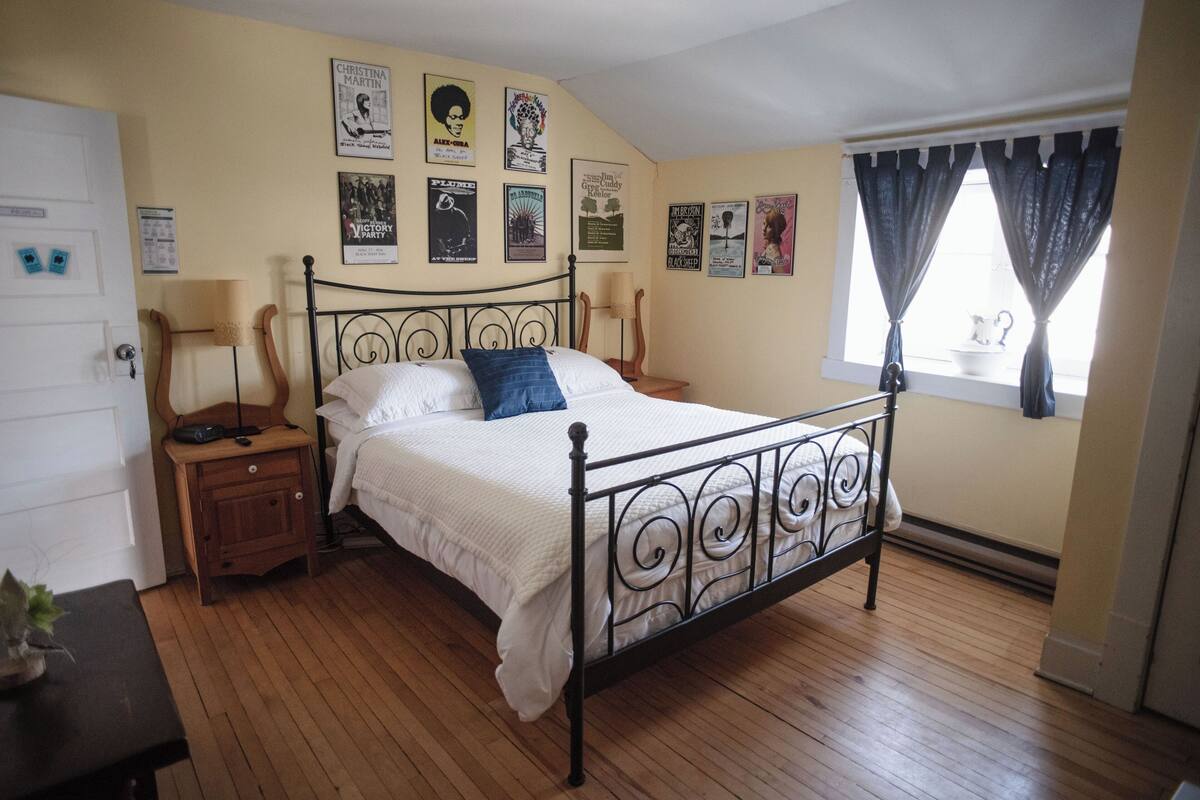 A bedroom with a metal bed frame, wooden floor, and a window with curtains.