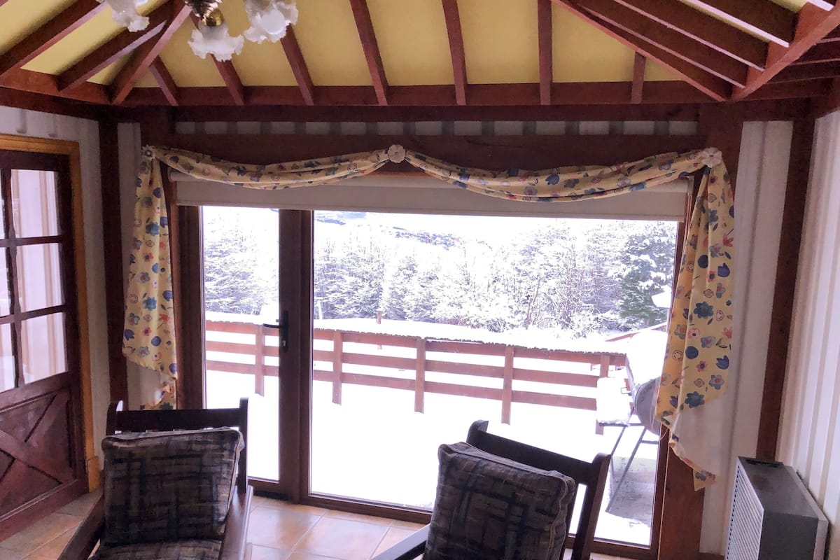 Une pièce avec un plafond en bois, une grande porte-fenêtre coulissante donnant sur un balcon et deux fauteuils à motifs écossais.