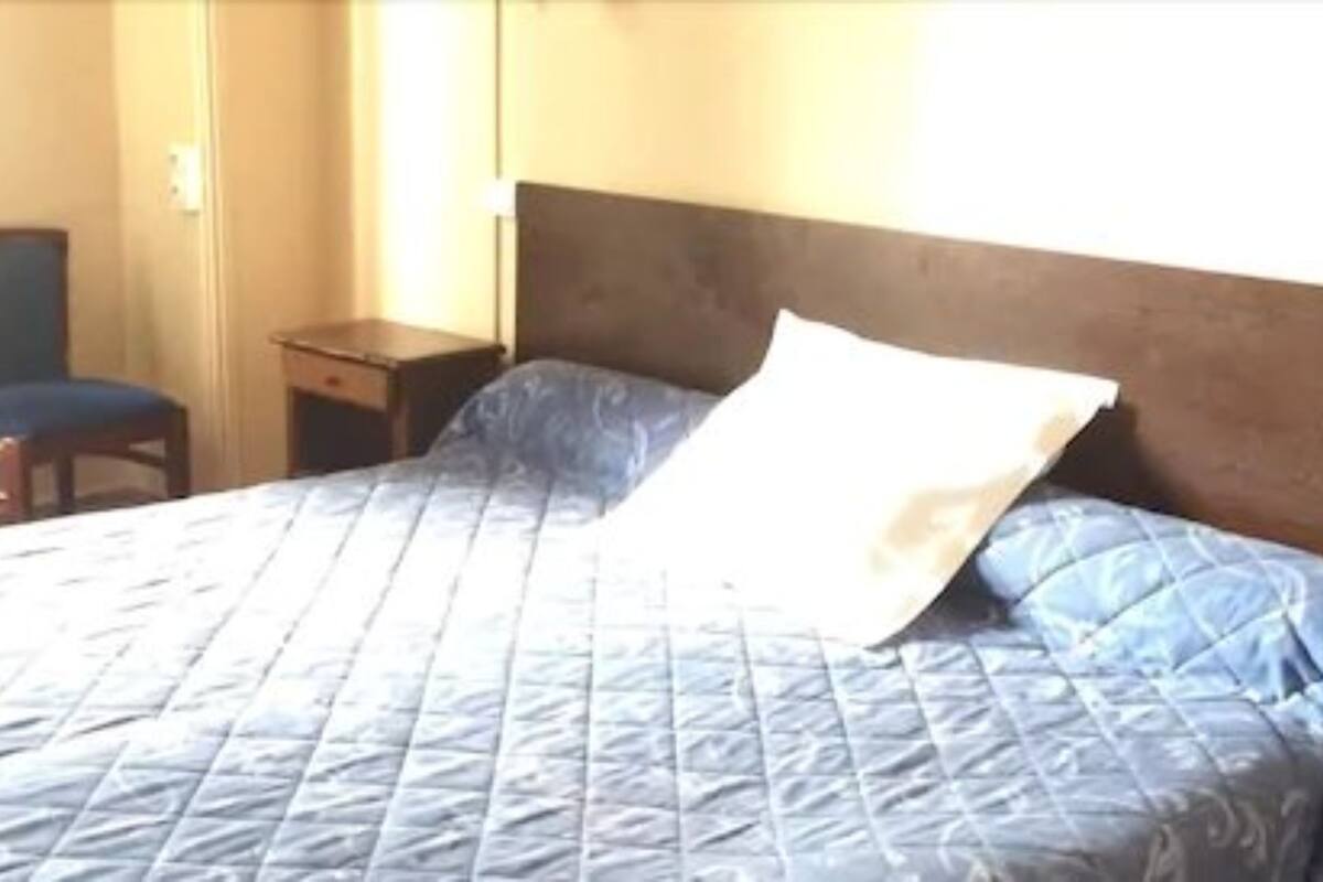 Una cama con cubrecama azul acolchado, una mesita de noche de madera y una silla.