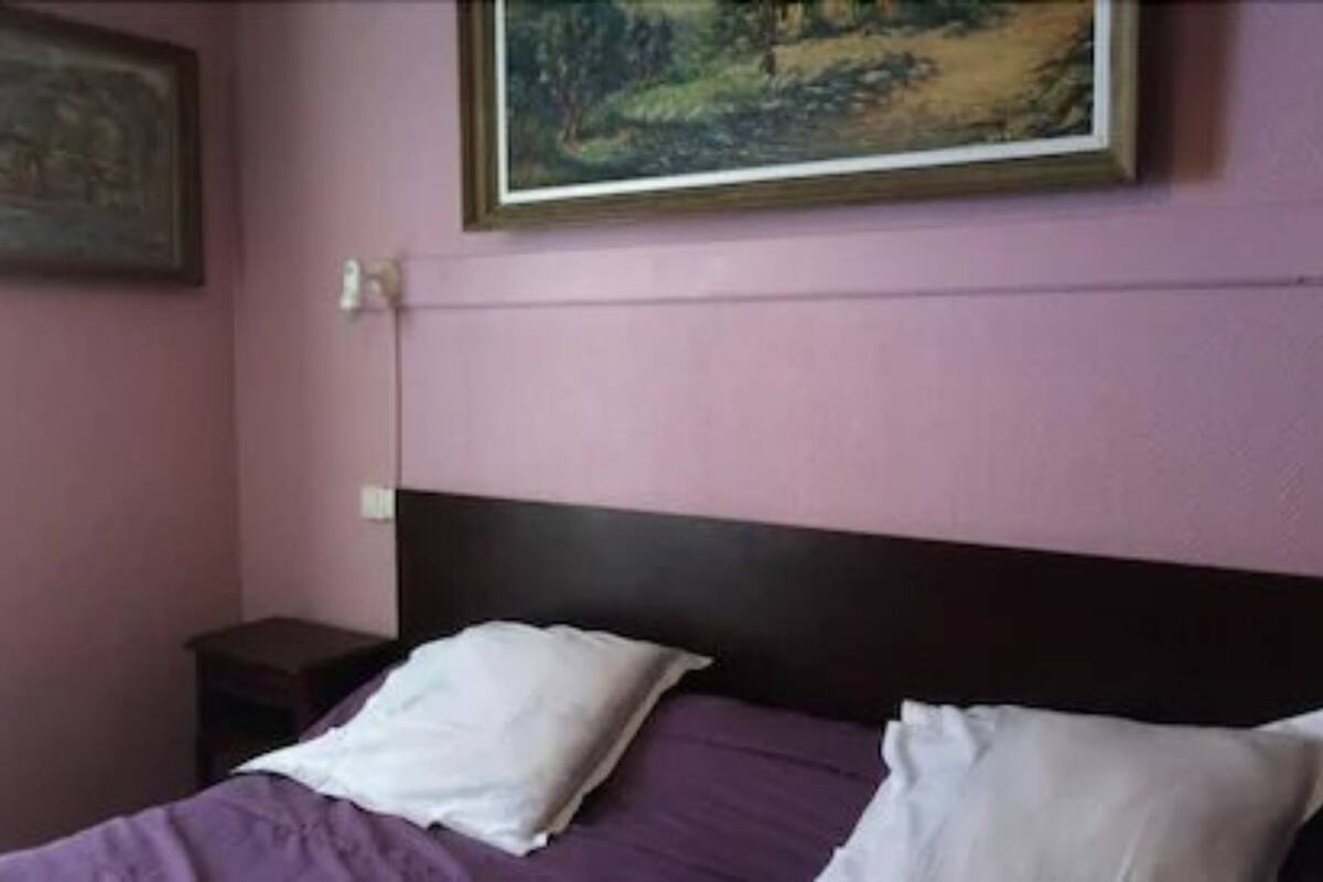Un dormitorio con cama, dos almohadas, una mesita de noche y un cuadro en la pared.