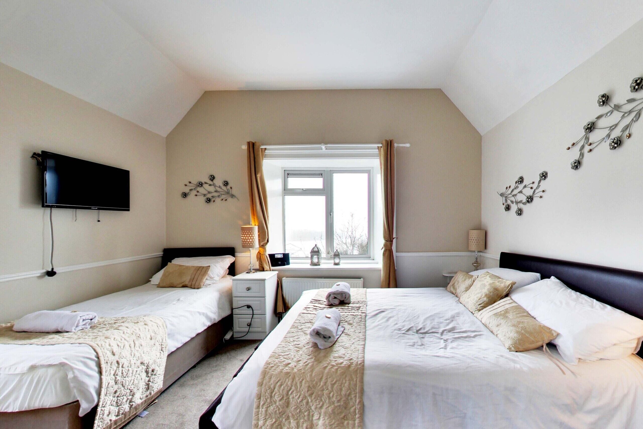 A hotel room with two beds, a TV, a window with curtains, and wall decor.