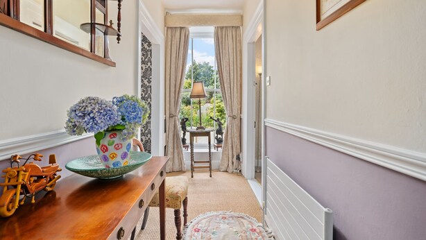 Un pasillo con una mesa de madera, un jarrón de flores y vista a un jardín a través de una puerta.